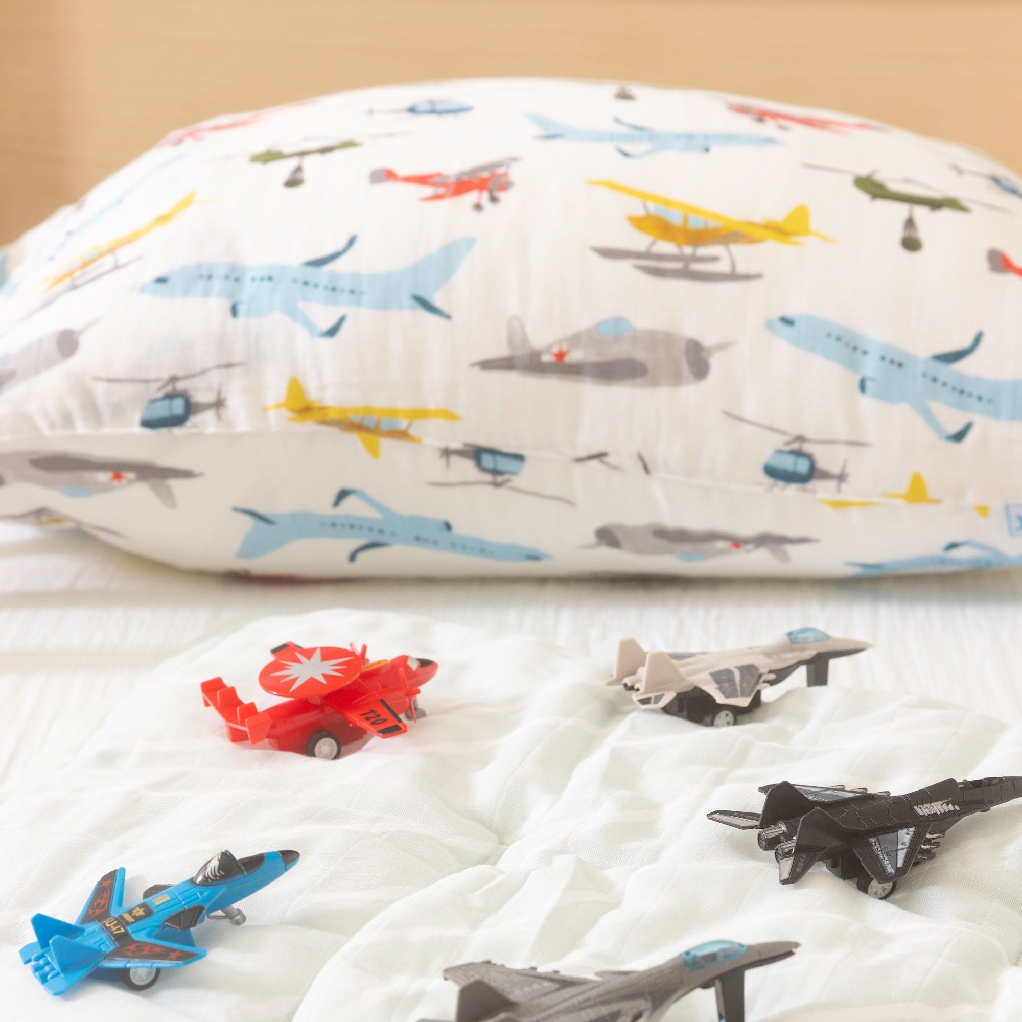 Colorful airplane-patterned pillowcase on a bed with toy airplanes.